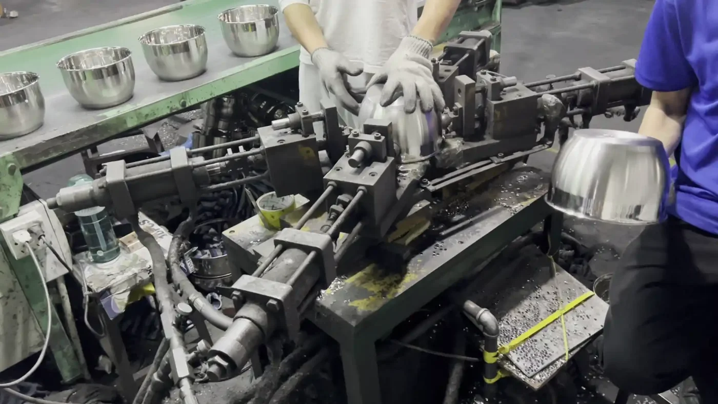 Workers positioning inverted cookware bodies for handle-hole preparation