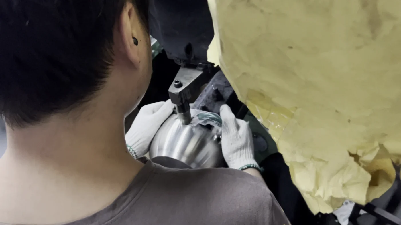 Worker holding a stainless steel cookware body at a handle attachment station
