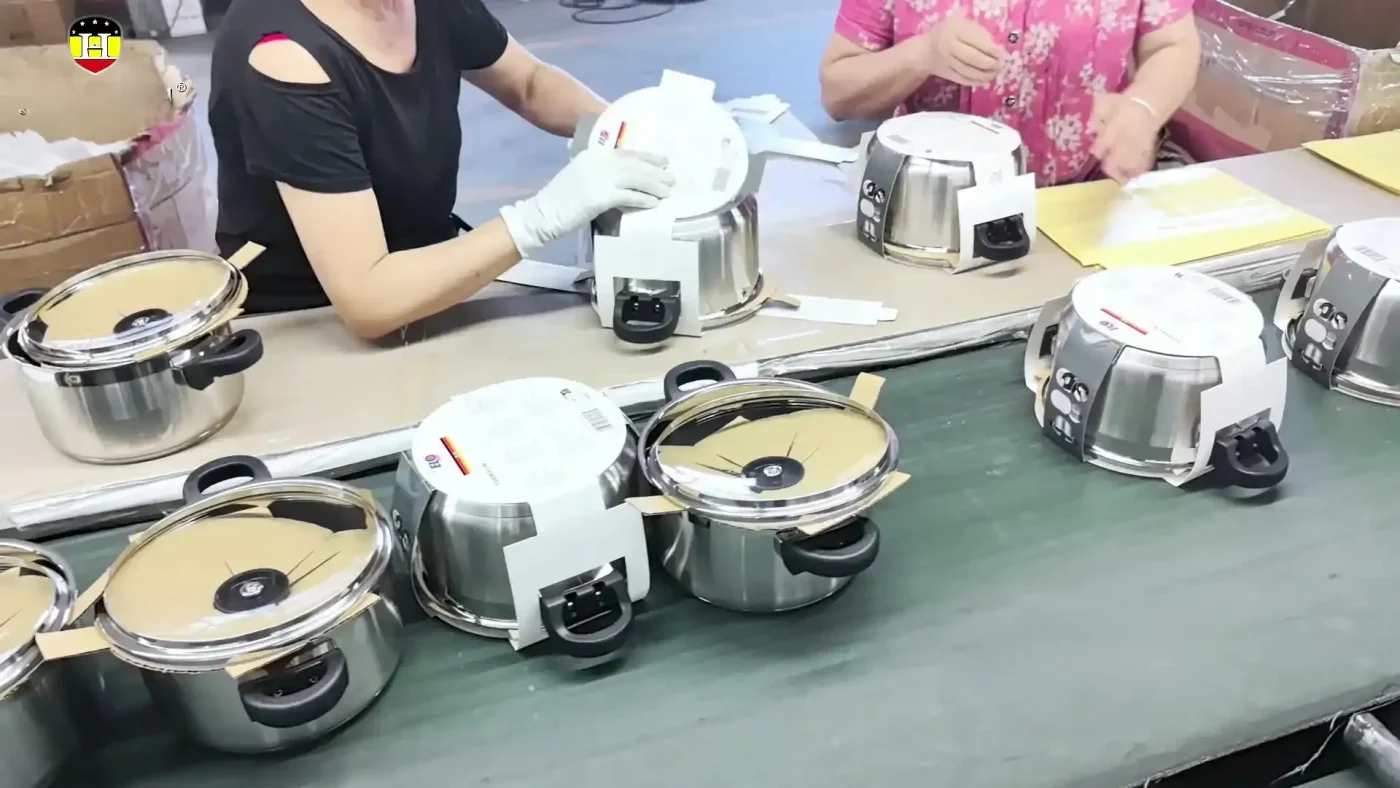 Workers fitting paper protectors around assembled cookware on a packing line